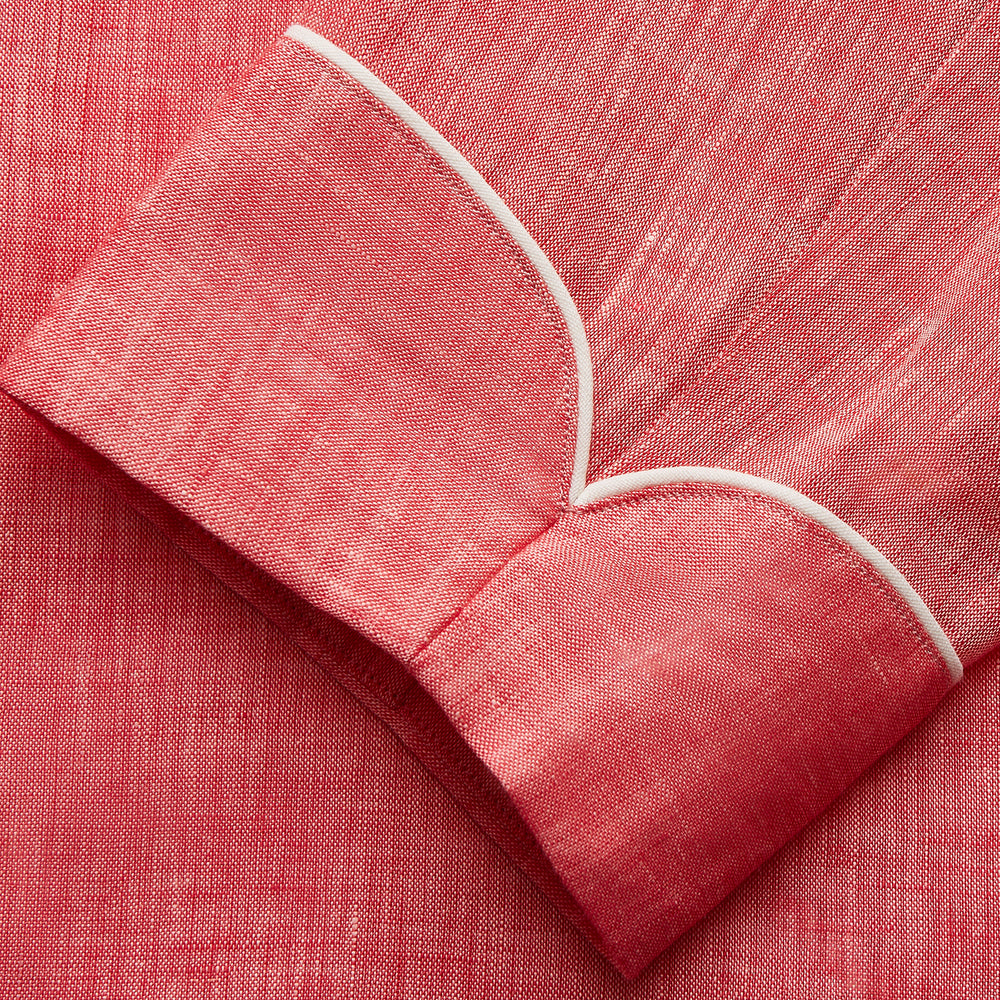 The Pink Linen Arnold Gown by Turnbull & Asser features white piping, long sleeves, a shawl collar, chest pocket, and a wrap-around belt tied at the waist, shown on a white background.
