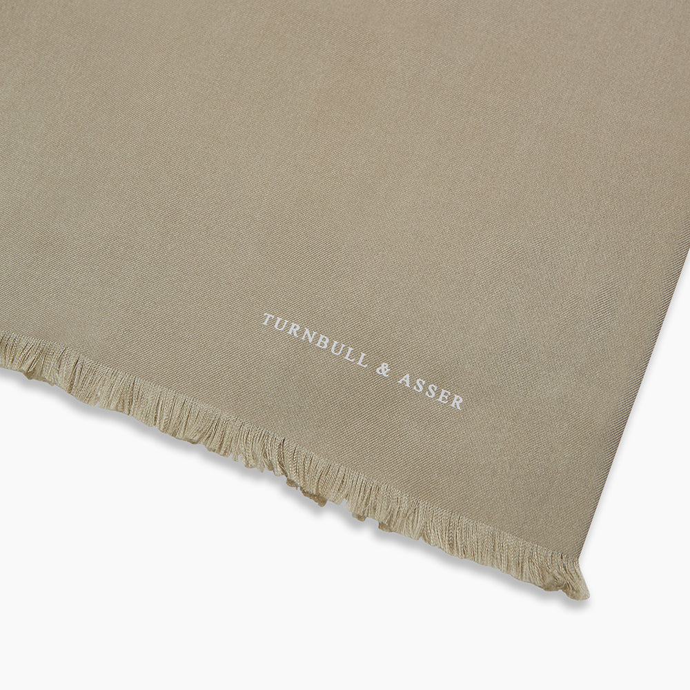 The Khaki Silk Twill Lawton Scarf by Turnbull & Asser, an essential accessory, features fringed edges and is neatly folded on a white background. A small logo near one end adds a refined Turnbull touch.