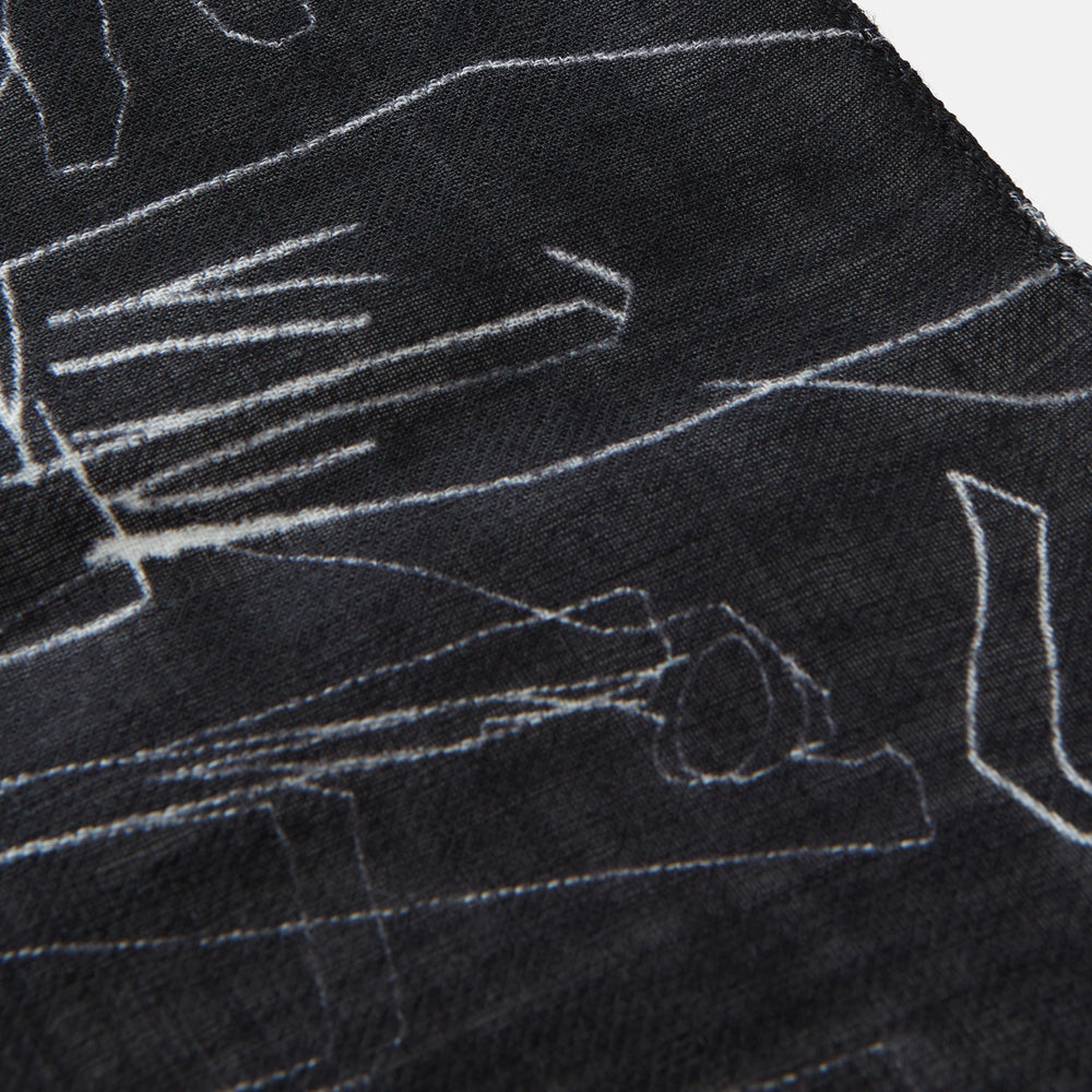 The Turnbull & Asser Black Sketched Pattern Wool Chilcott Scarf features white abstract lines, frayed edges, and is shown loosely knotted on a light gray background.