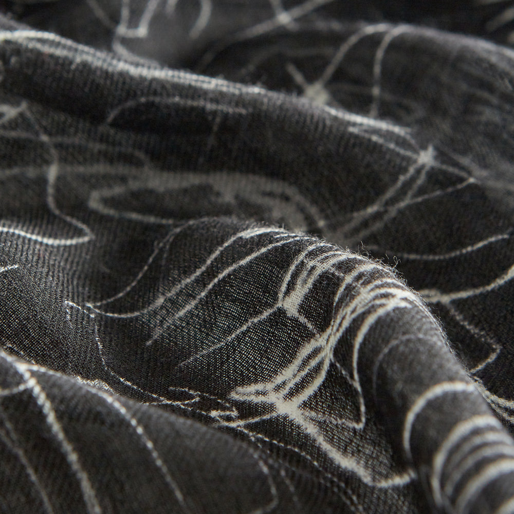The Turnbull & Asser Black Sketched Pattern Wool Chilcott Scarf features white abstract lines, frayed edges, and is shown loosely knotted on a light gray background.