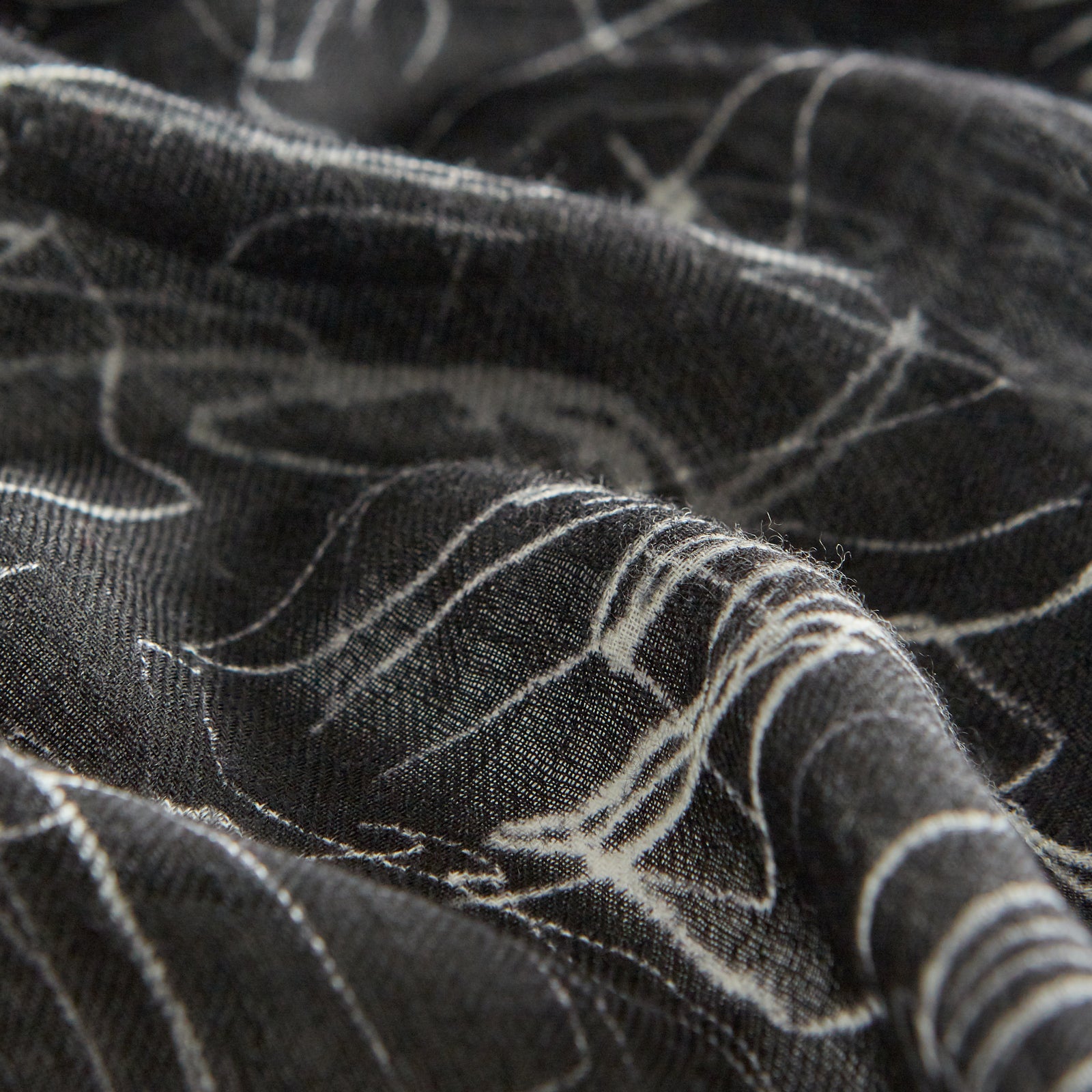 View 4 of product The Turnbull & Asser Black Sketched Pattern Wool Chilcott Scarf features white abstract lines, frayed edges, and is shown loosely knotted on a light gray background.