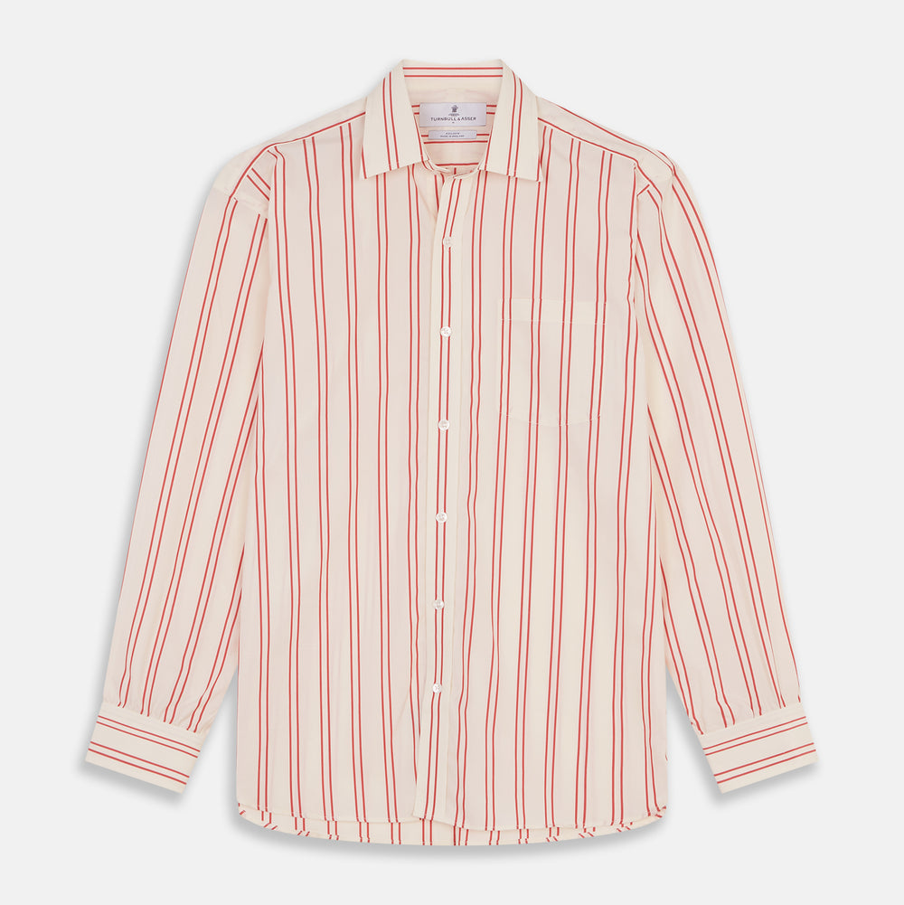 A man poses against a beige backdrop in the Turnbull & Asser Red and Off-White Stripe Cotton Weekend Fit Finch Shirt, styled with dark blue jeans and a brown belt for a timeless look. One hand rests in his pocket as he faces slightly to the side.