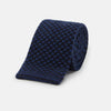 View 1 of product The Turnbull & Asser Navy Multi Cashmere Knitted Tie features a subtle black checkered pattern and is shown rolled up against a plain light background.