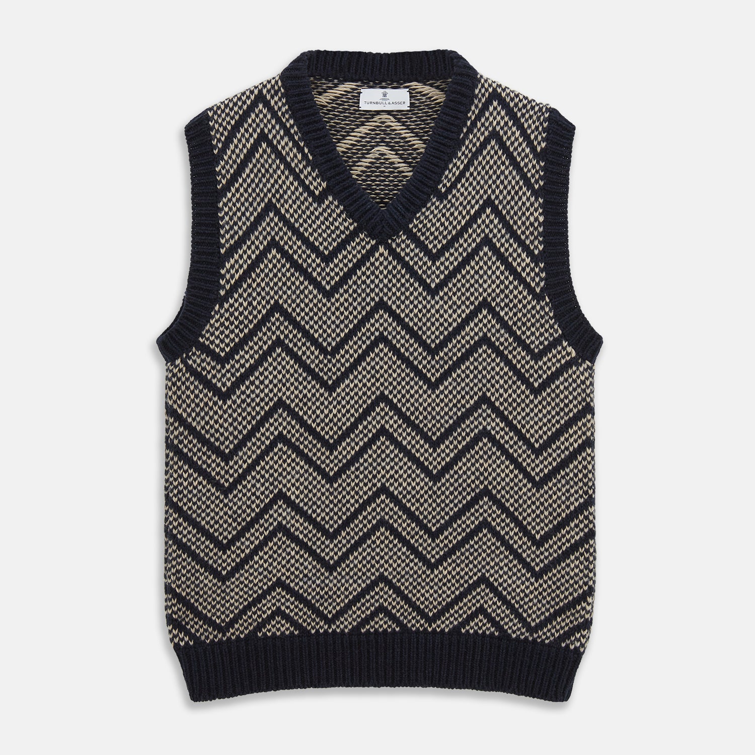 View 1 of product The Turnbull & Asser Navy and White Wool Blend Albion Chunky Slipover is a sleeveless knitted vest with ribbed V-neck, armholes, and hem, featuring a bold chevron pattern.
