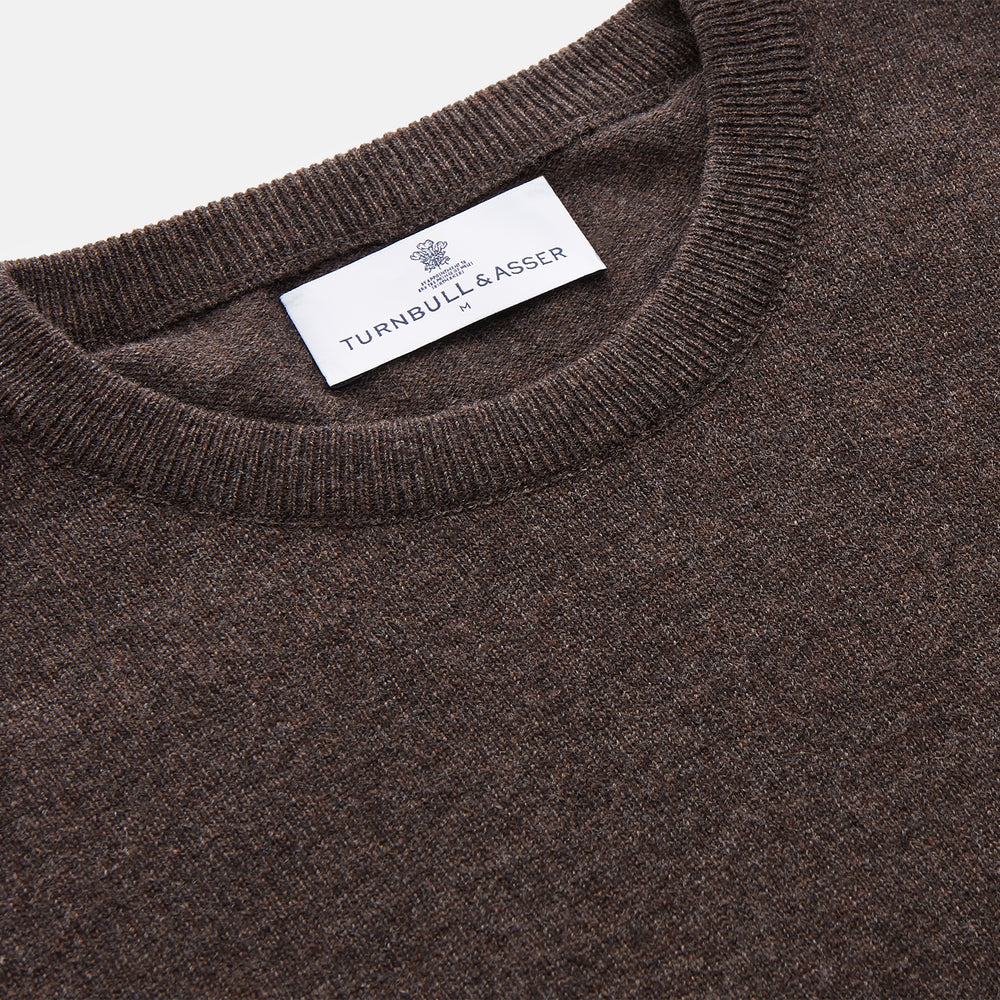 The Turnbull & Asser Brown Cashmere Glenn Jumper is a classic menswear piece with a crew neck and ribbed cuffs, collar, and hem. It’s laid flat on a white background, showcasing its timeless long-sleeved design.