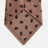 View 3 of product The Bronze and Chocolate Brown Tile Silk Tie by Turnbull & Asser features a classic tile pattern with small black graduation caps, neatly rolled on a plain white background.