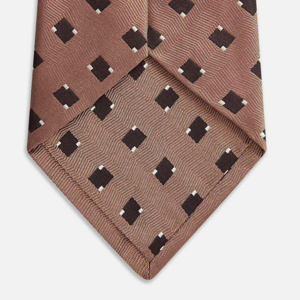 The Bronze and Chocolate Brown Tile Silk Tie by Turnbull & Asser features a classic tile pattern with small black graduation caps, neatly rolled on a plain white background.
