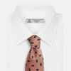 View 4 of product The Bronze and Chocolate Brown Tile Silk Tie by Turnbull & Asser features a classic tile pattern with small black graduation caps, neatly rolled on a plain white background.