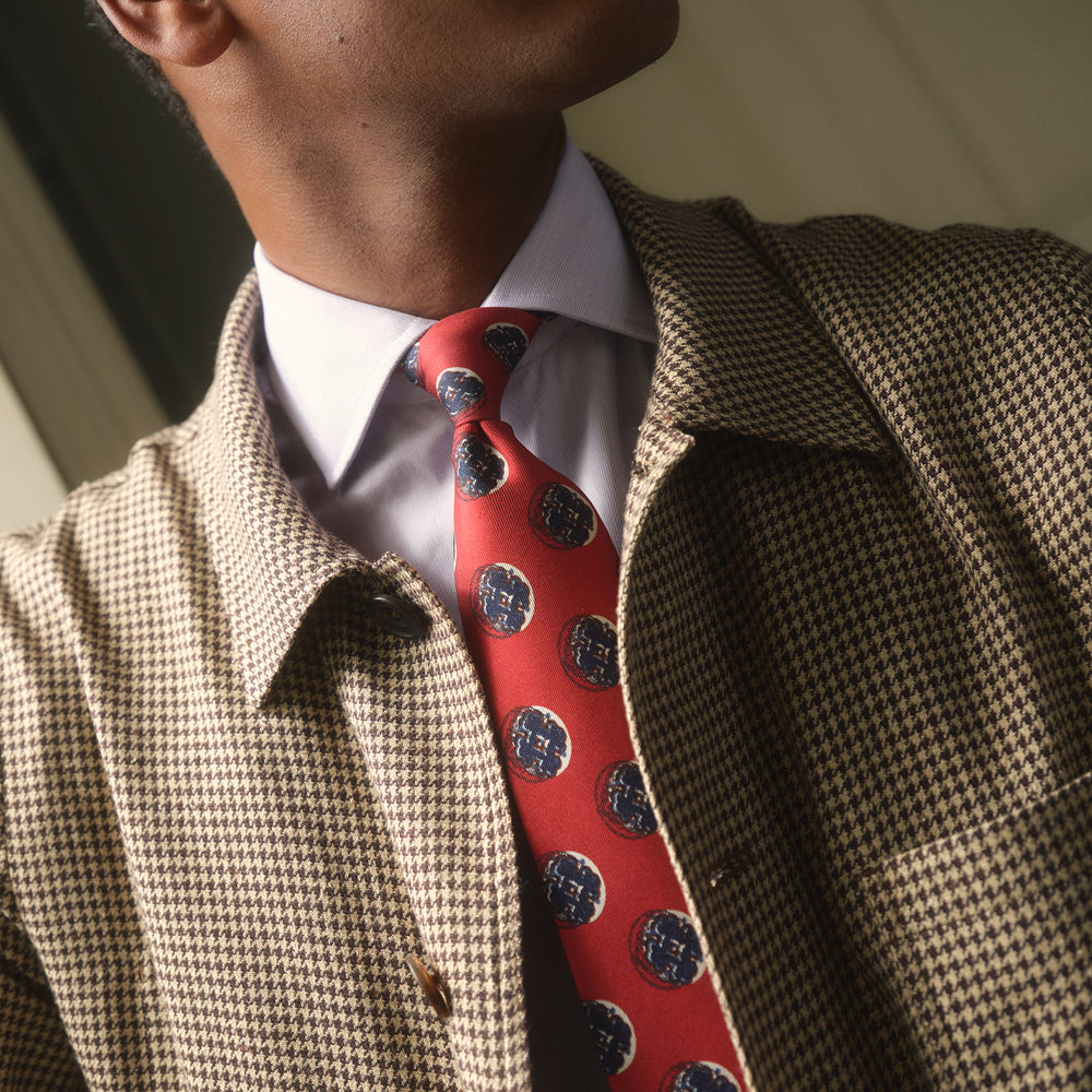 A rolled-up Red Shadow Spot Printed Silk Tie by Turnbull & Asser, showcasing large navy blue and white circular motifs, displayed on a plain white background.