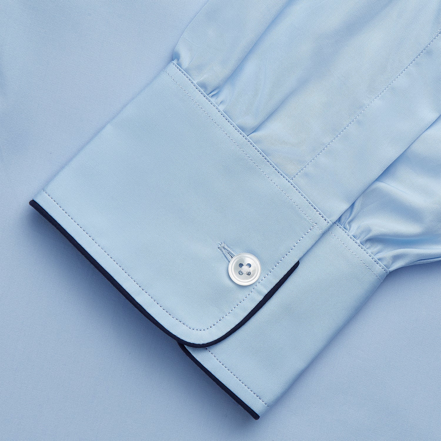 View 4 of product The Turnbull & Asser Light Blue Piped Cotton Nightshirt is a luxurious long-sleeve shirt dress with a pointed collar, black piping on the collar, cuffs, and chest pocket, button front closure, and curved hem.