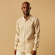 A man with a bald head and trimmed beard wears the Turnbull & Asser Beige Weekend Fit Linen Blake Shirt with stand collar and 1-button cuffs, standing calmly against a matching beige background.
