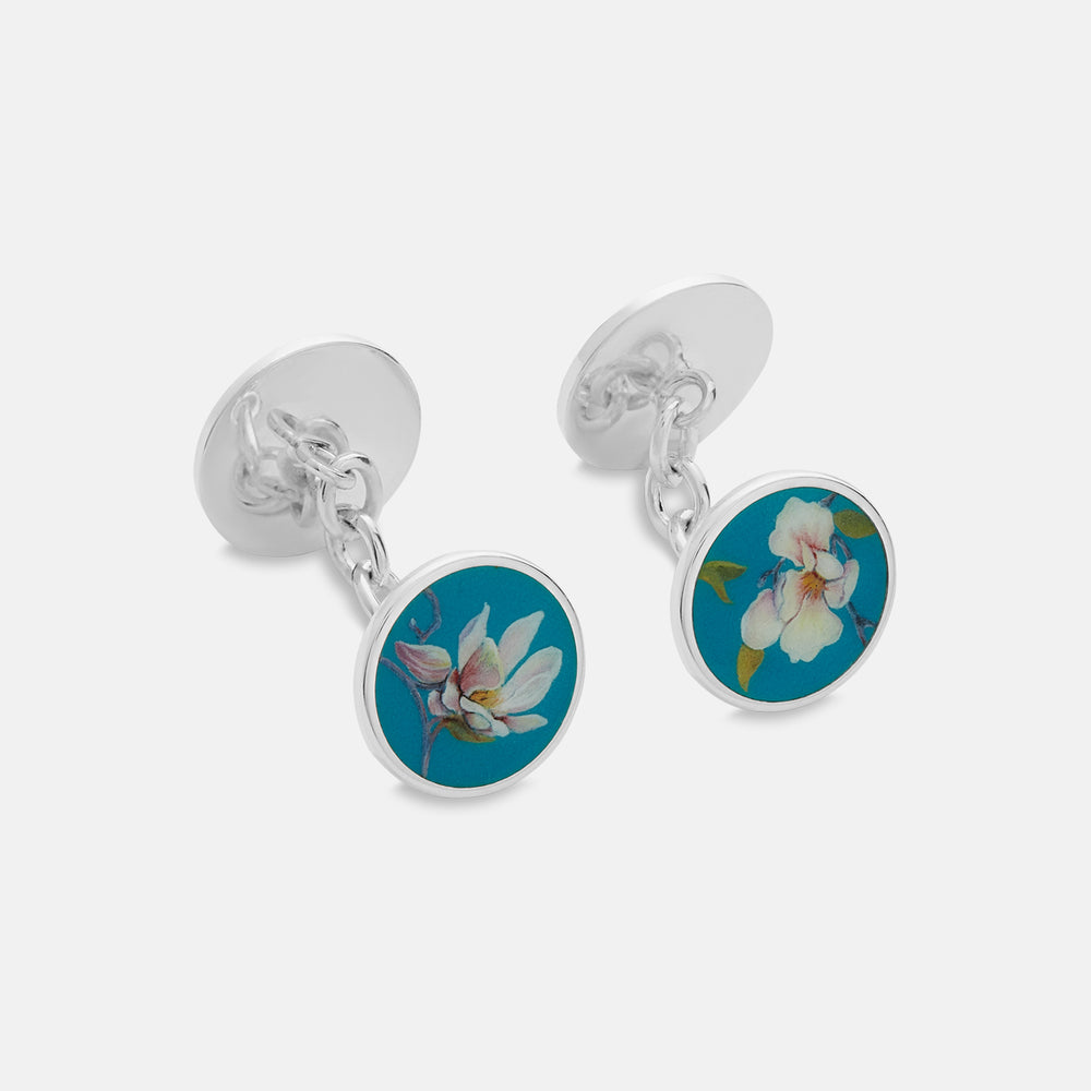 Turnbull & Asser’s Teal Magnolia Hand-painted Cufflinks feature circular sterling silver faces with magnolia designs on a teal background. Each handmade pair is shown on a plain white surface.