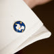 A close-up of a white shirt cuff adorned with Turnbull & Asser’s Royal Blue Magnolia Hand-painted Cufflink, featuring a blue background and white flower design with yellow and brown accents.