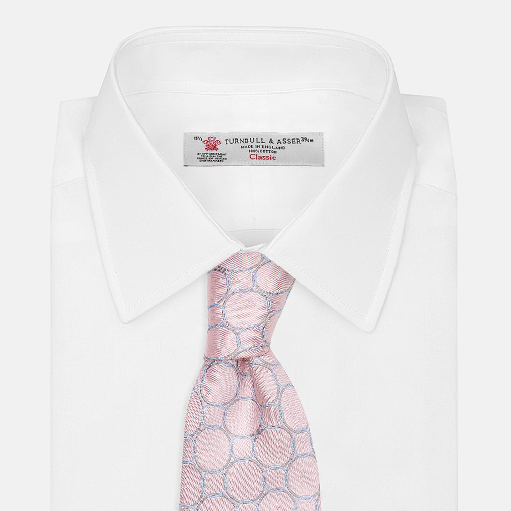 The Turnbull & Asser Baby Pink and Blue Circle Jacquard Silk Tie features a subtle geometric pattern, elegantly rolled against a plain white background.