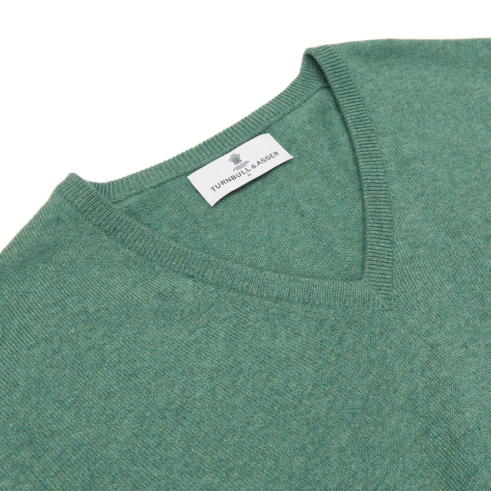 The Turnbull & Asser Green Cashmere V-Neck Jumper features long sleeves, ribbed cuffs and hem, and is styled in classic Scottish knitwear, shown flat against a white background.