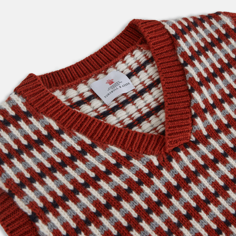 The Rust Knitted Cashmere Slipover by Turnbull & Asser is a sleeveless V-neck vest in red, white, and dark brown houndstooth, inspired by Welsh knitwear with solid red ribbed trim at the collar, armholes, and hem.