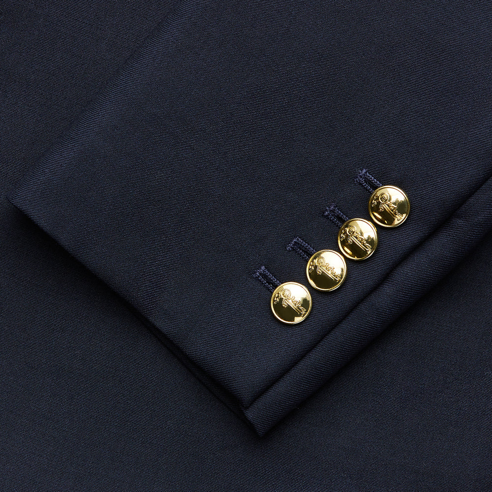 The Turnbull & Asser Navy Plain Wool Single Breasted Blazer features brass buttons on the front and cuffs, notched lapels, and multiple front pockets, shown laid flat against a white background.