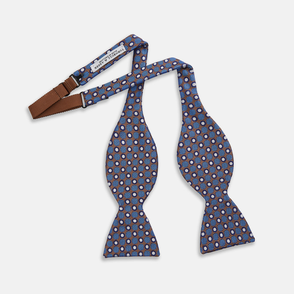 The Turnbull & Asser Brown and Blue Circle and Spot Silk Bow Tie features a blue silk base with light blue and brown circular dots on textured fabric, shown against a white background.