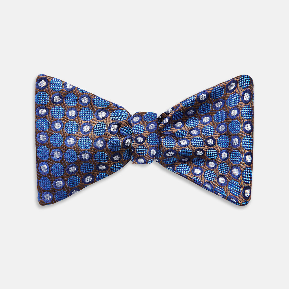 The Turnbull & Asser Brown and Blue Circle and Spot Silk Bow Tie features a blue silk base with light blue and brown circular dots on textured fabric, shown against a white background.
