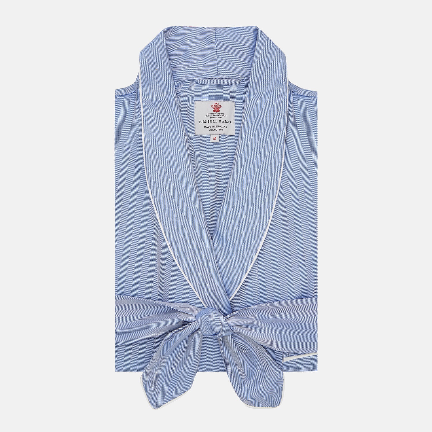 View 1 of product The Blue Herringbone Superfine Cotton Gown by Turnbull & Asser is a folded light blue robe with white piping and a tied front belt, featuring a branded collar label, displayed against a plain white background.