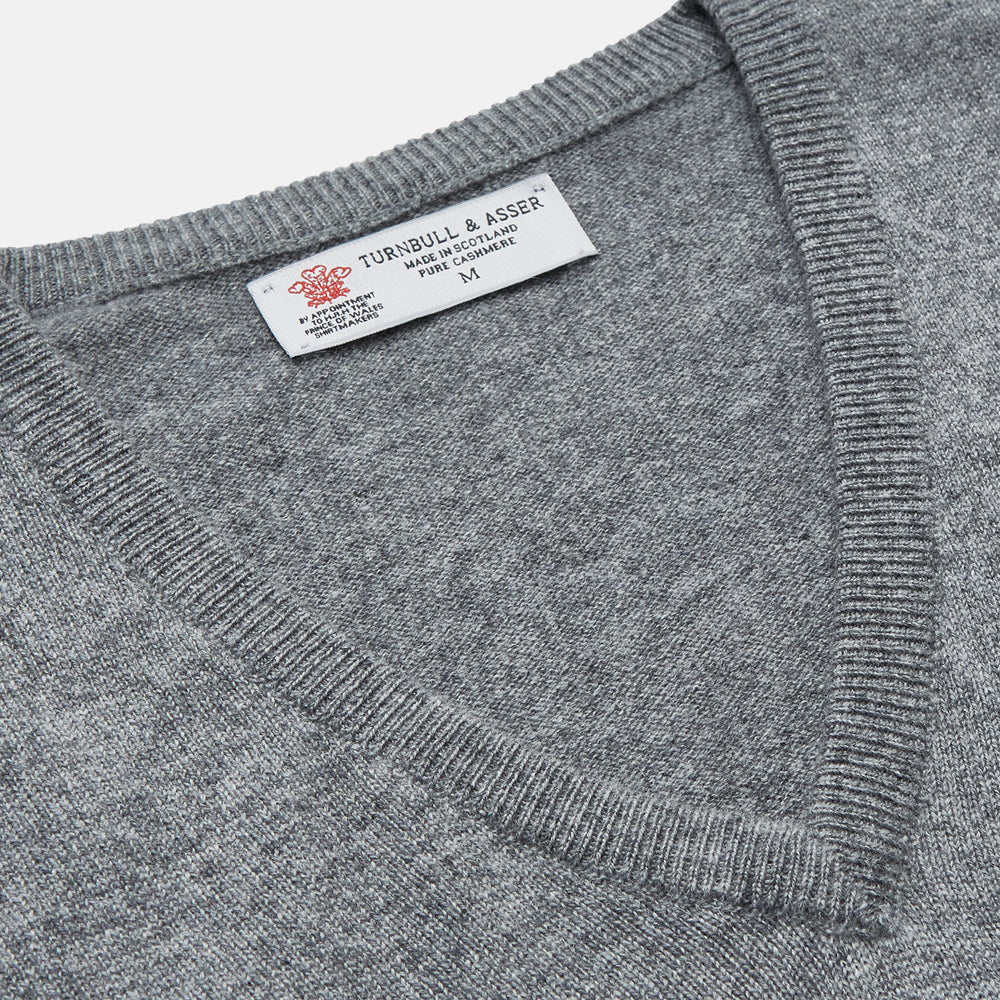 The Turnbull & Asser Flannel Grey V-Neck Cashmere Jumper, shown laid flat on a white background, features long sleeves and ribbed cuffs, hem, and neckline for a classic look with no visible patterns or embellishments.