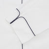 View 2 of product Turnbull & Asser's White Sea Island Cotton Pyjama Set, featuring a folded white men's top with dark piping and a matching face mask, is showcased on a plain white background.