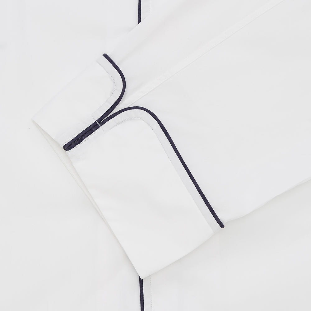Turnbull & Asser's White Sea Island Cotton Pyjama Set, featuring a folded white men's top with dark piping and a matching face mask, is showcased on a plain white background.