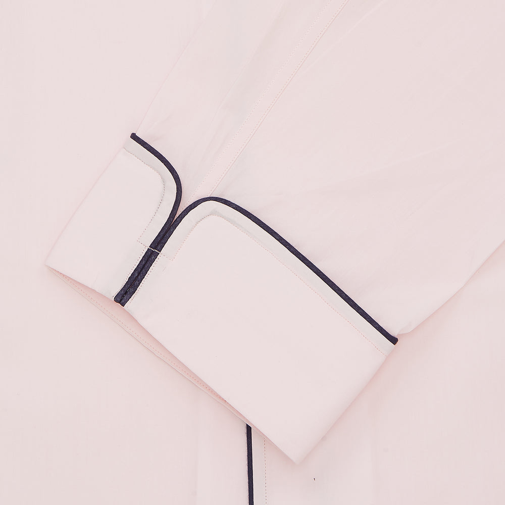 The Pink Sea Island Cotton Pyjama Set by Turnbull & Asser features a folded light pink top with black piping and white buttons, shown beside a matching headscarf with two ties, highlighting luxury men’s sleepwear on a white background.