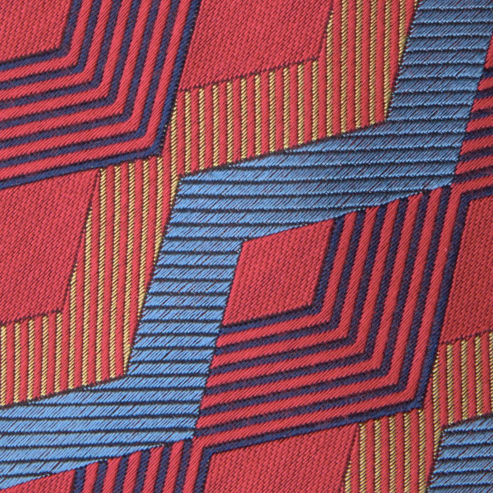 The Turnbull & Asser Red and Blue Zig Zag Silk Tie is a limited-run silk tie featuring interlocking geometric zigzag shapes and diagonal stripes in red, blue, gold, and navy.