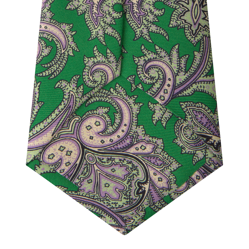 The Turnbull & Asser Green and Purple Large Paisley Printed Silk Tie features a light purple and white intricate paisley pattern, rolled up and set against a plain white background for timeless style.