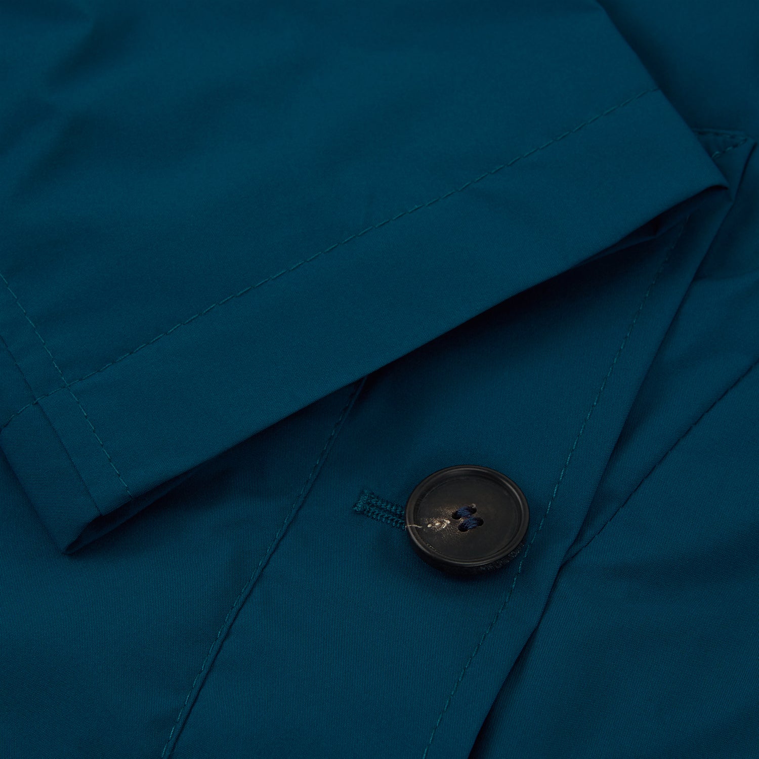 View 2 of product The Turnbull & Asser Blue Pack-Away Rain Mac is a knee-length coat with a classic collar, long sleeves, side buttoned pockets, and a concealed front placket, shown against a plain white background.