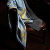 View 2 of product The Pale Blue Wool and Cashmere Lily Blanket by Turnbull & Asser features abstract, hand-drawn designs in blue, yellow, and gray on a white background.