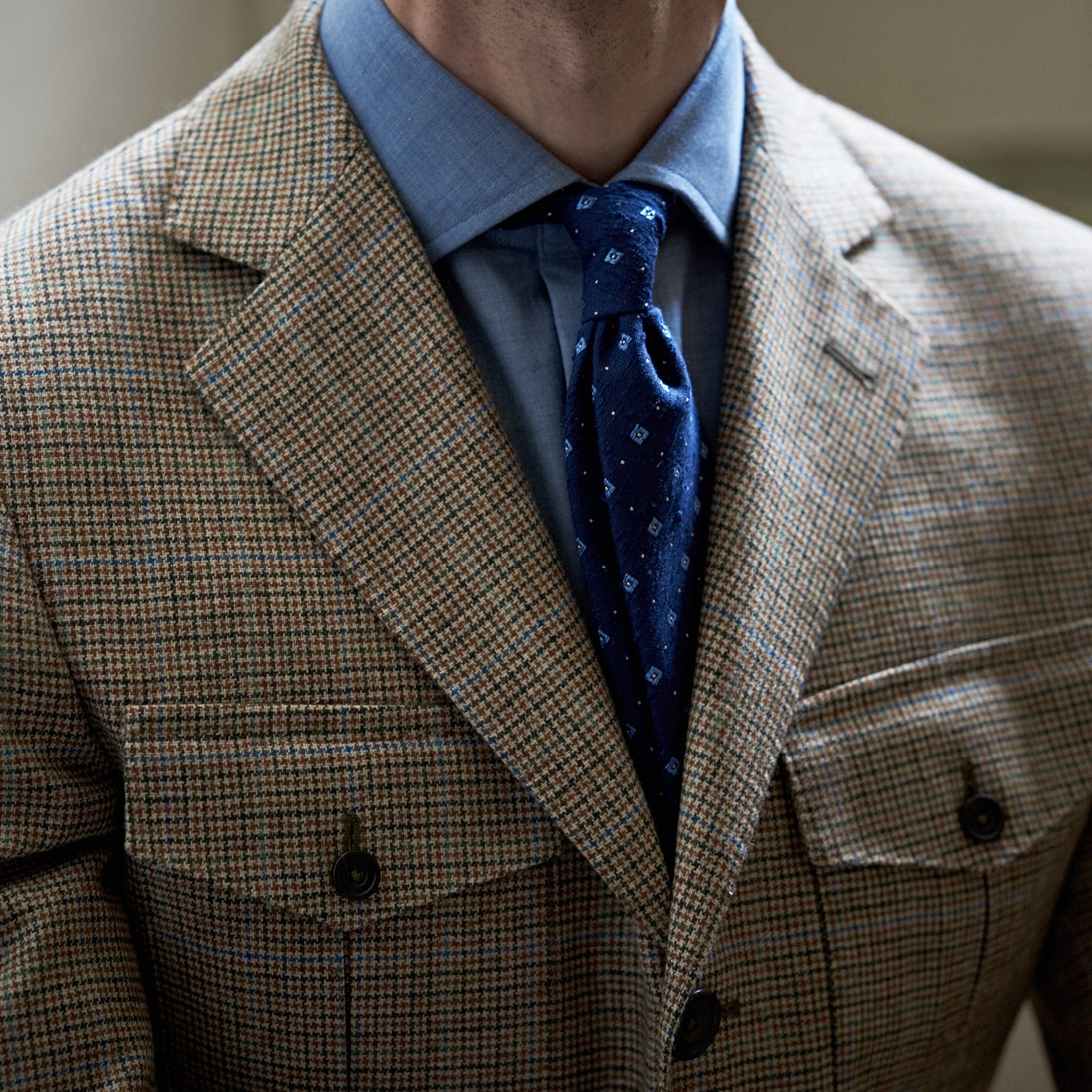 View 2 of product The Byron Wool Check Travel Jacket by Turnbull & Asser features a brown plaid pattern, notched lapel, four flap utility pockets, and dark buttons. This lightweight wool jacket is shown on a plain white background.
