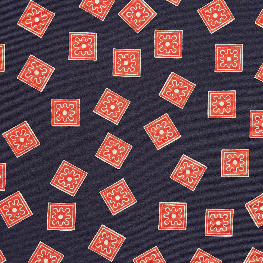 The Navy and Cherry Red Tiled Floral Silk Pocket Square by Turnbull & Asser features a blue background with red and white geometric floral patterns, a decorative border, and the brand's name in one corner.