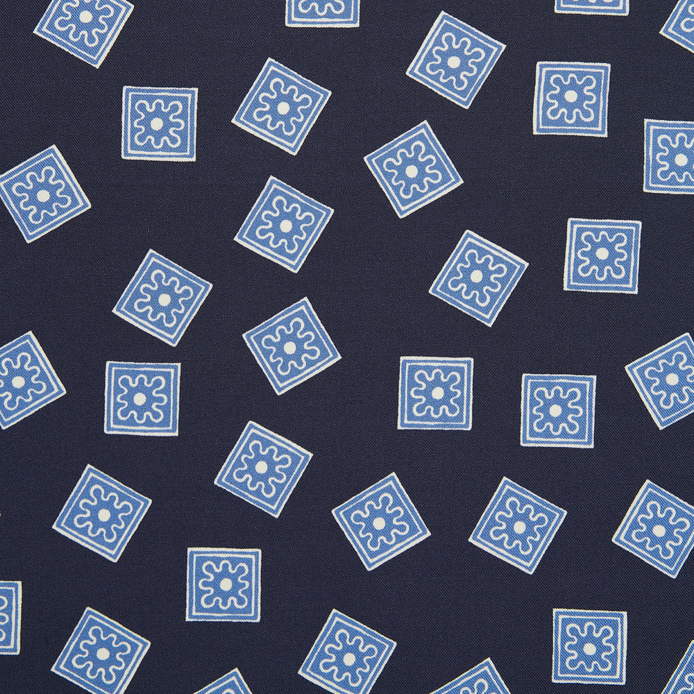 The Navy and Sky Blue Tiled Floral Silk Pocket Square by Turnbull & Asser features a geometric floral pattern in blue and white, a detailed border, and the brand's logo in the bottom right corner.