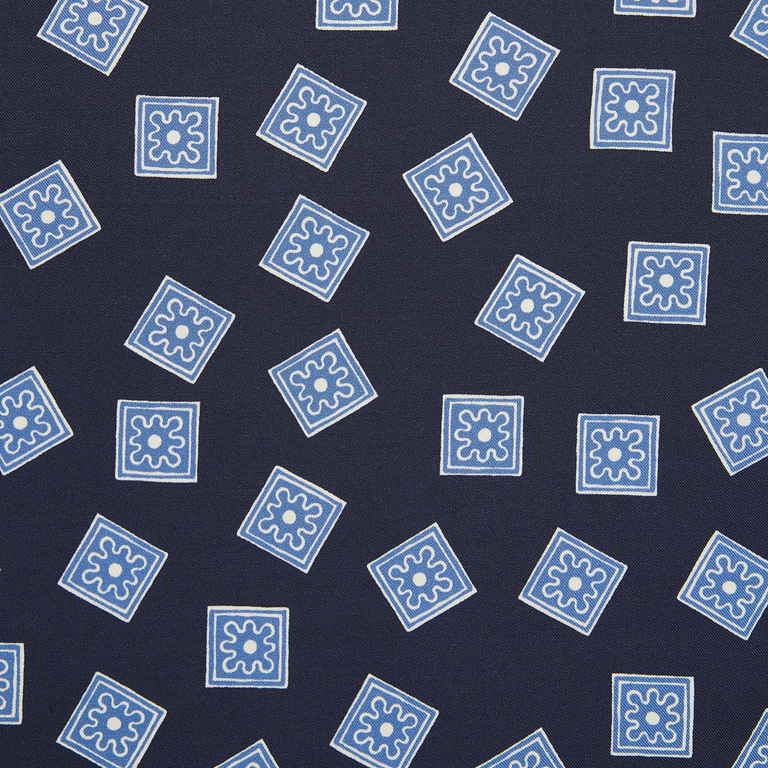 View 2 of product The Navy and Sky Blue Tiled Floral Silk Pocket Square by Turnbull & Asser features a geometric floral pattern in blue and white, a detailed border, and the brand's logo in the bottom right corner.