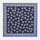 The Navy and Sky Blue Tiled Floral Silk Pocket Square by Turnbull & Asser features a geometric floral pattern in blue and white, a detailed border, and the brand's logo in the bottom right corner.
