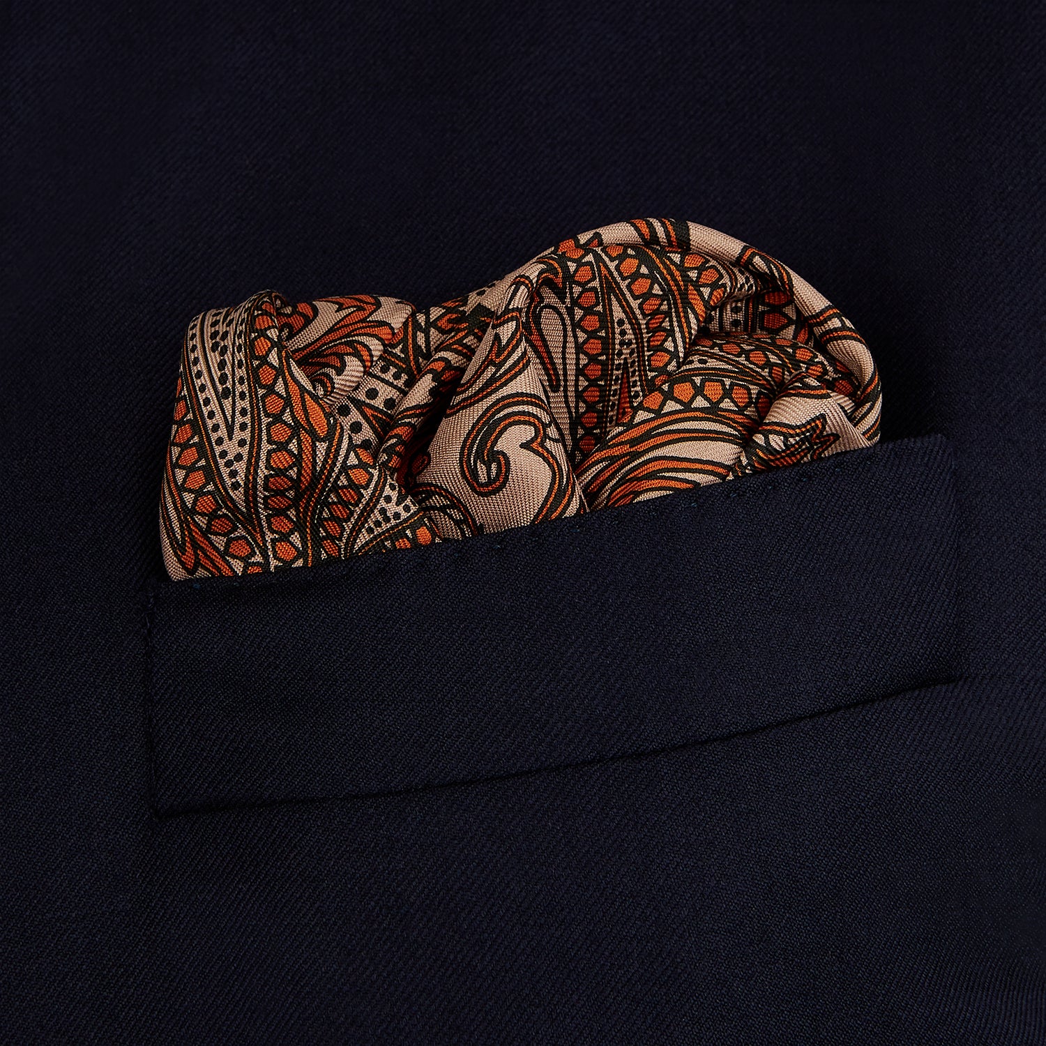 View 3 of product The Orange House Paisley Print Silk Pocket Square by Turnbull & Asser features a brown paisley design on a light brown silk background with a solid brown border and brand's logo printed in one corner.