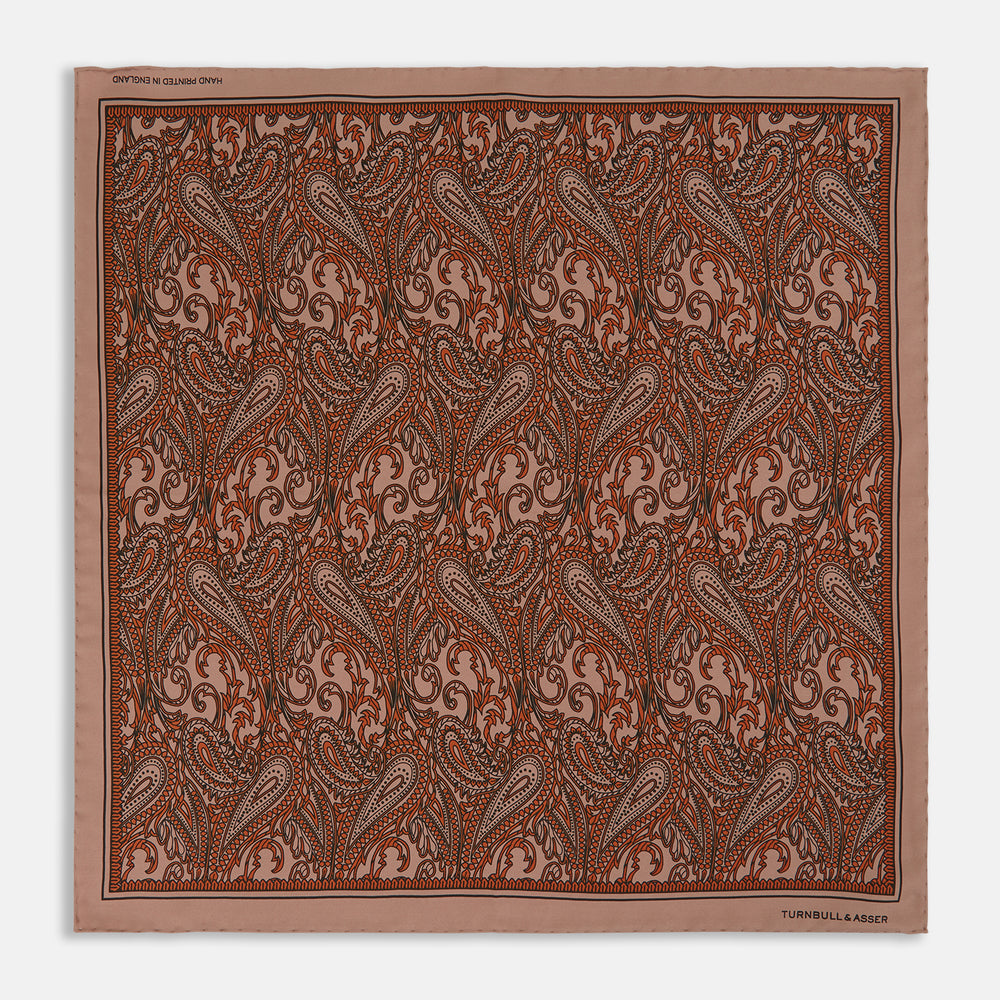 The Orange House Paisley Print Silk Pocket Square by Turnbull & Asser features a brown paisley design on a light brown silk background with a solid brown border and brand's logo printed in one corner.