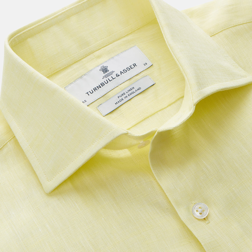 A man stands against a beige background, wearing the Turnbull & Asser Cream Tailored Fit Shelton Shirt with a Kent collar and black pants. He faces forward with a neutral expression, his arms relaxed by his sides.