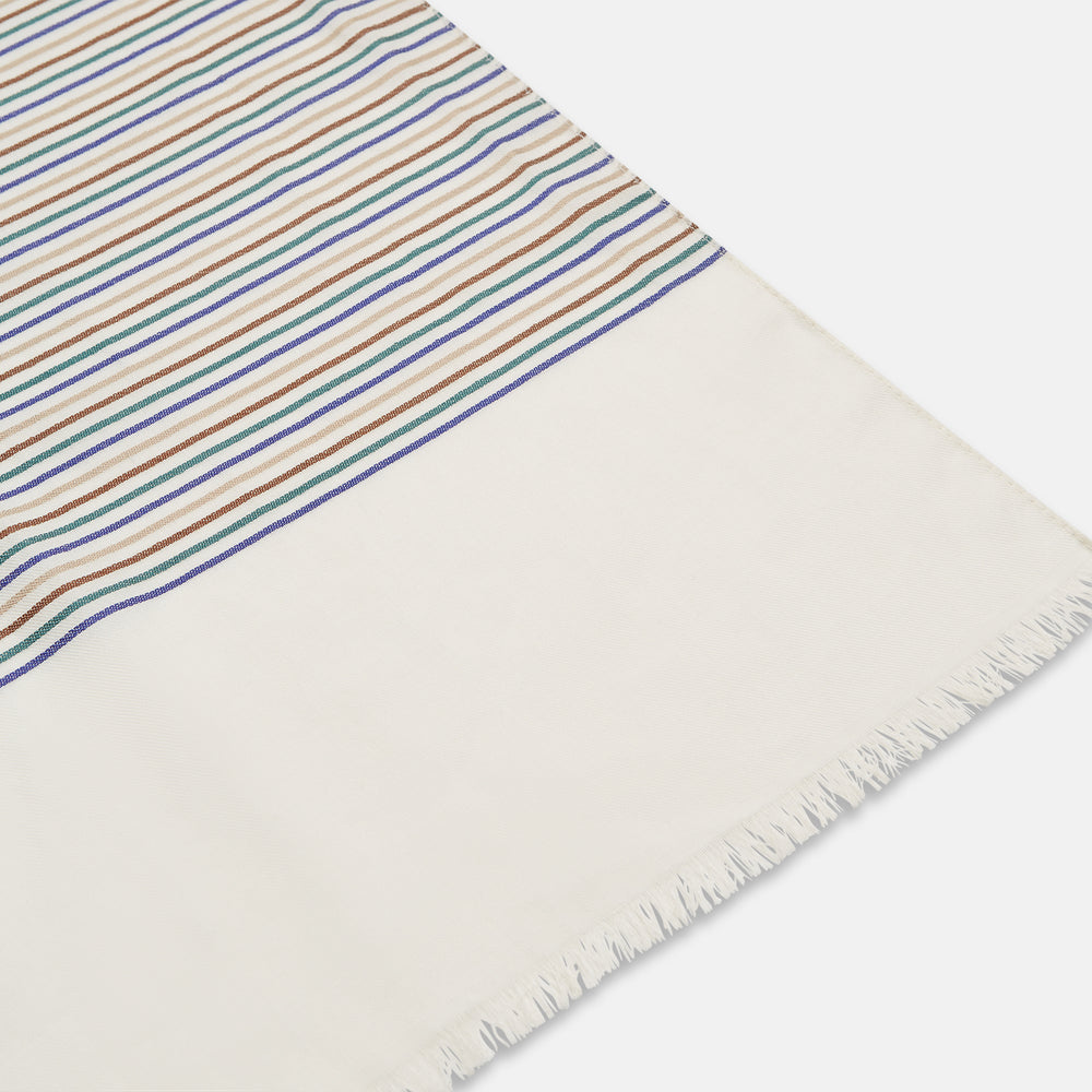 A man wearing a Turnbull & Asser Cream Abstract Stripe Print Lightweight Wool Scarf and a beige shirt stands outside by a tree, surrounded by greenery, gazing thoughtfully to the side.
