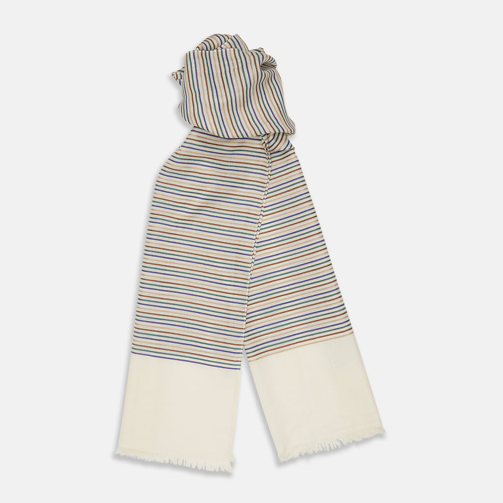 A man wearing a Turnbull & Asser Cream Abstract Stripe Print Lightweight Wool Scarf and a beige shirt stands outside by a tree, surrounded by greenery, gazing thoughtfully to the side.