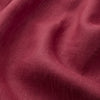 View 3 of product A person stands barefoot against a plain background, wearing the Turnbull & Asser Burgundy Linen Piped Gown belted at the waist over blue pajamas, looking to the side with one hand in the gown’s pocket.