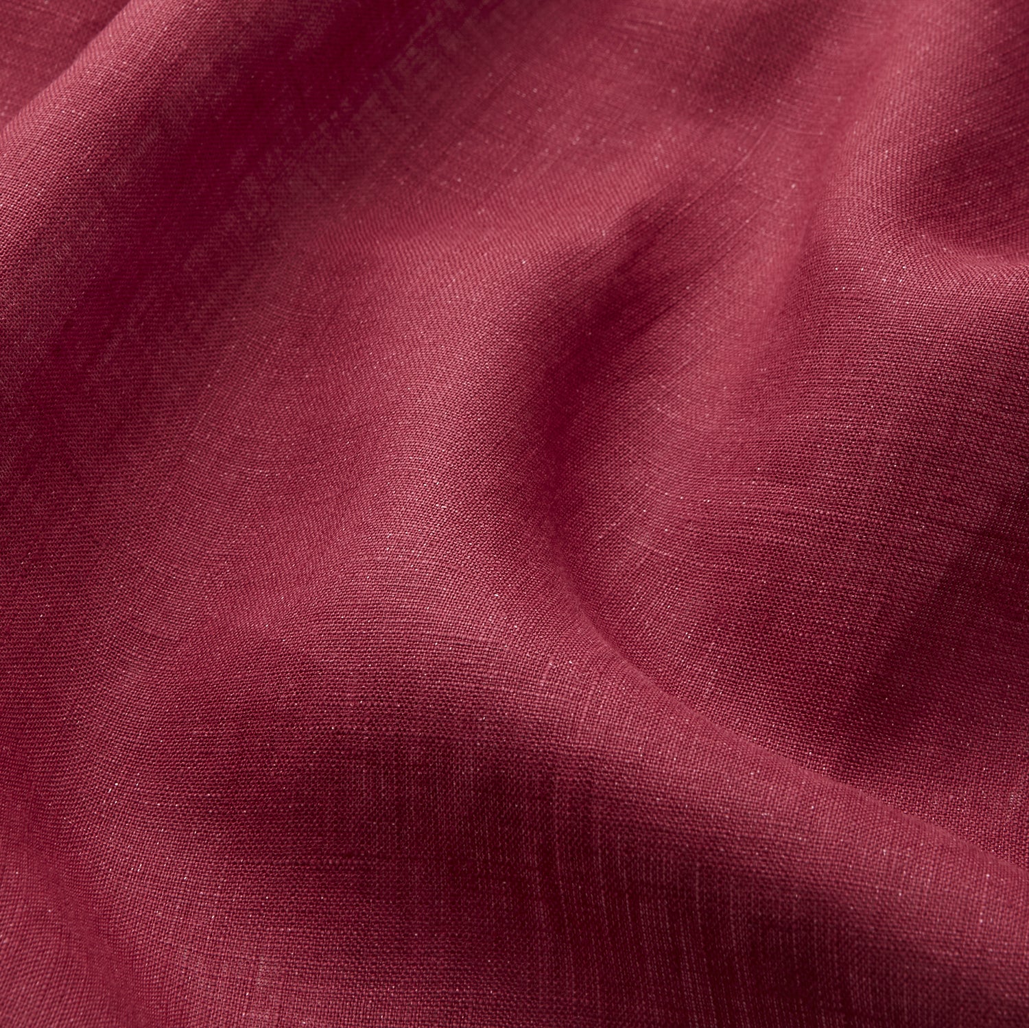 View 3 of product A person stands barefoot against a plain background, wearing the Turnbull & Asser Burgundy Linen Piped Gown belted at the waist over blue pajamas, looking to the side with one hand in the gown’s pocket.