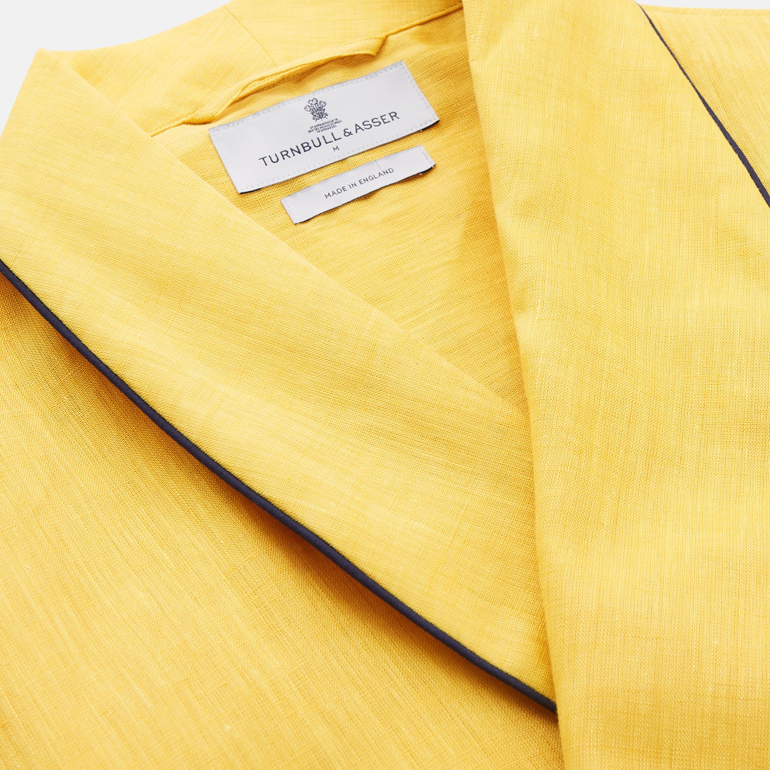 View 5 of product The Turnbull & Asser Ochre Linen Piped Gown features black piping on the collar, cuffs, and edges, a chest pocket, two front pockets, and a matching waist belt. Made with breathable linen for comfort, shown against a plain white background.