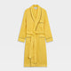 The Turnbull & Asser Ochre Linen Piped Gown features black piping on the collar, cuffs, and edges, a chest pocket, two front pockets, and a matching waist belt. Made with breathable linen for comfort, shown against a plain white background.