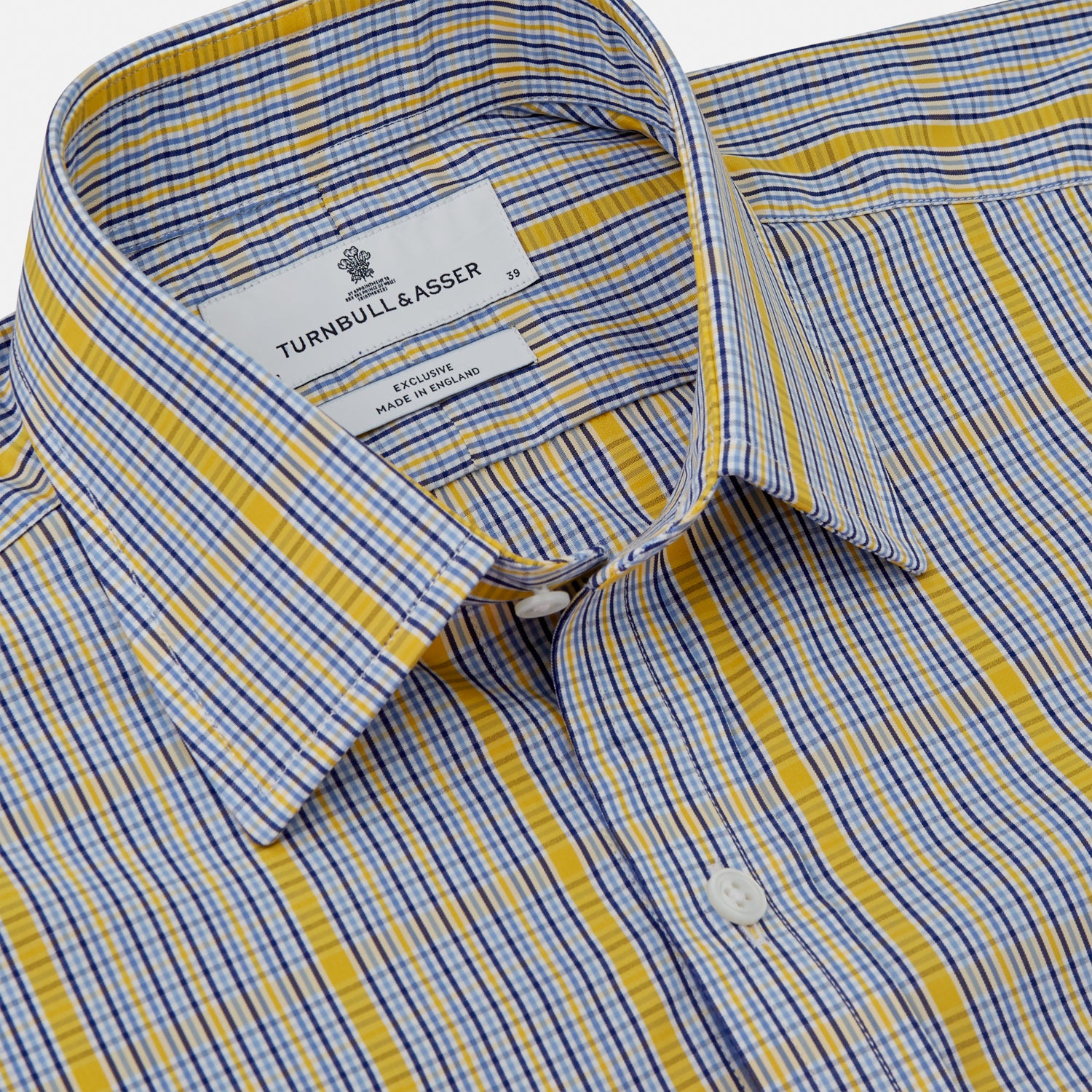 View 4 of product A man stands against a light background, wearing a Turnbull & Asser Yellow and Blue Fancy Check Regular Fit Shirt with T&A Collar, a patterned tie, dark dress pants, and black shoes. He faces forward with hands in pockets and a neutral expression.