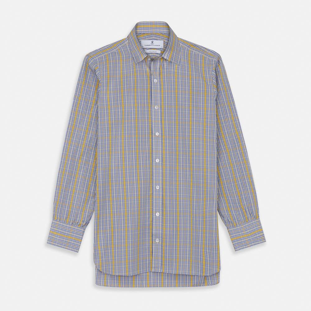 A man stands against a light background, wearing a Turnbull & Asser Yellow and Blue Fancy Check Regular Fit Shirt with T&A Collar, a patterned tie, dark dress pants, and black shoes. He faces forward with hands in pockets and a neutral expression.