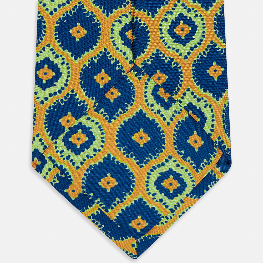 The Yellow Medallion Printed Silk Tie by Turnbull & Asser features a bold abstract medallion pattern in blue, green, and orange on yellow silk, displayed rolled up against a plain white background.