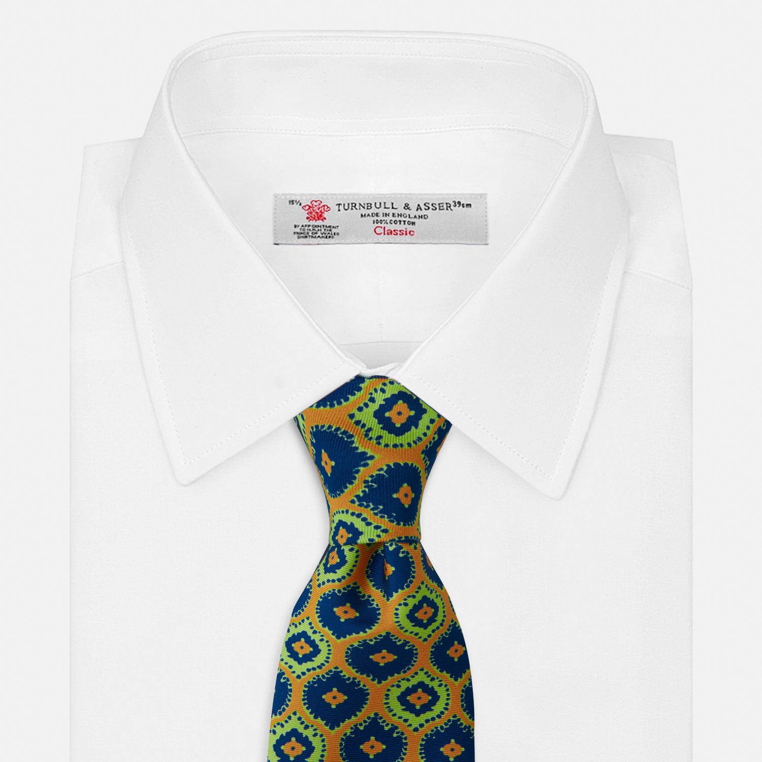 View 2 of product The Yellow Medallion Printed Silk Tie by Turnbull & Asser features a bold abstract medallion pattern in blue, green, and orange on yellow silk, displayed rolled up against a plain white background.